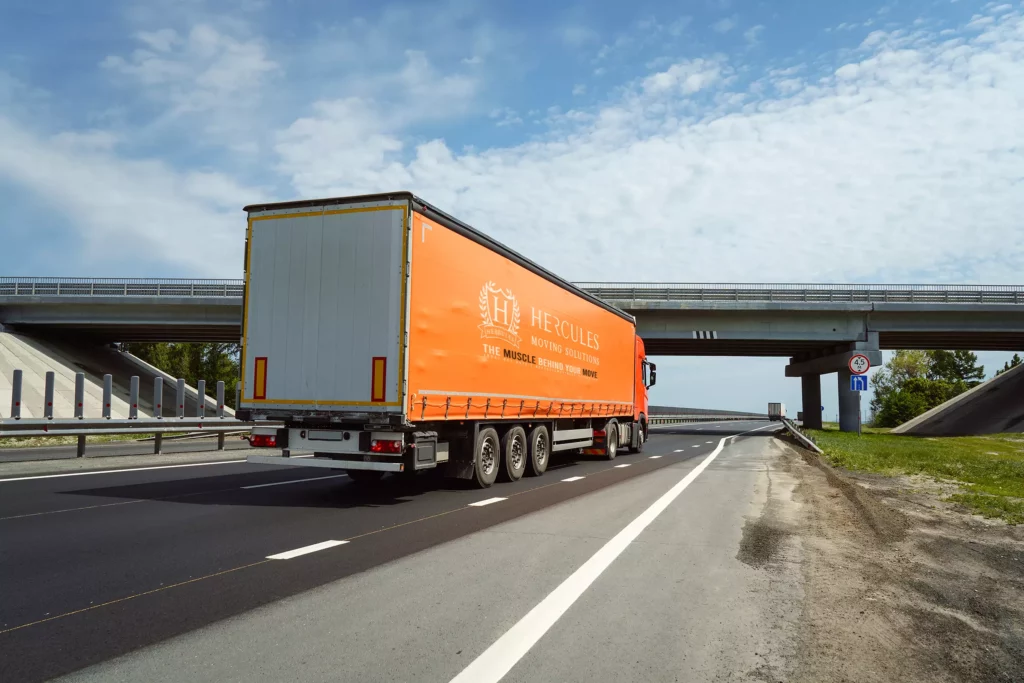 Freight truck driving on an open highway under a blue sky, representing long-distance moving and transportation services.