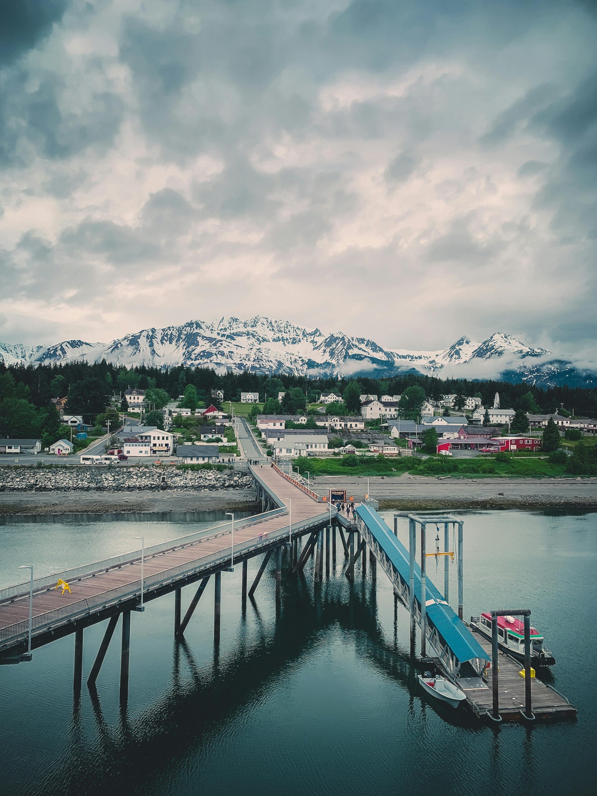 Dock and pier leading to a small coastal town in Alaska with snow-covered mountains in the background.