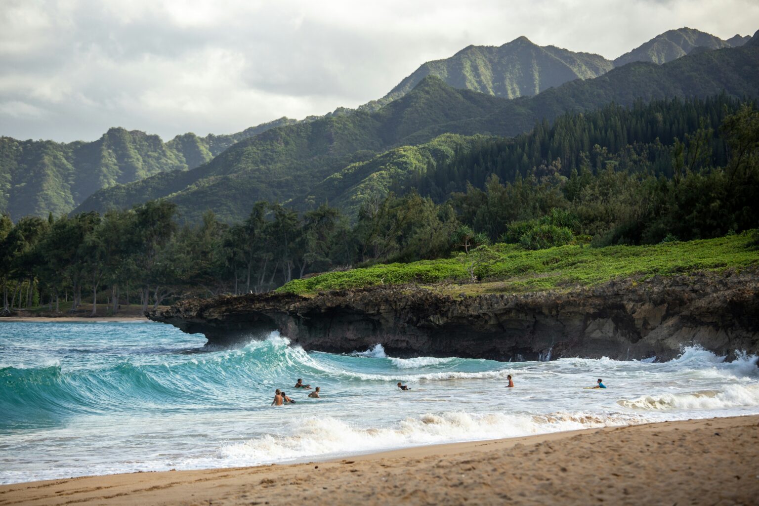 Hawaii beach with turquoise waves, rocky shoreline, and lush green mountains in the background.