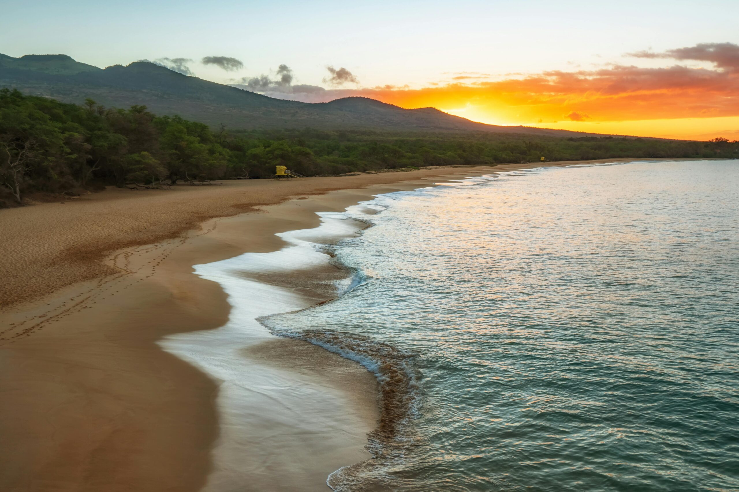 Quiet Hawaii beach at sunrise with gentle waves and mountains in the background.