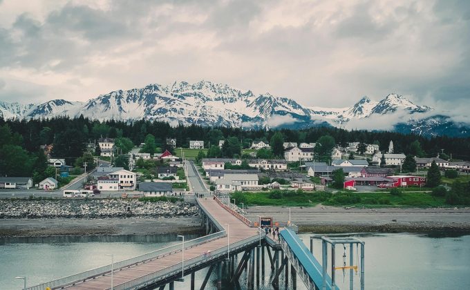 Dock and pier leading to a small coastal town in Alaska with snow-covered mountains in the background.